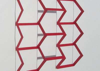 A modern geometric bookshelf with a red frame and transparent back, featuring a series of interlocking hexagonal and rectangular shapes against a plain background.