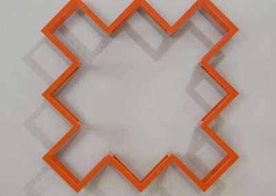 An orange, zigzag-shaped art frame mounted on a white wall, creating a continuous angular pattern around an empty central space.