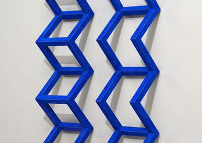 A three-dimensional wall sculpture featuring a series of interconnected blue geometric shapes that create an optical illusion, mounted on a white wall.