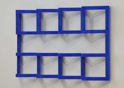 A blue geometric wall sculpture featuring a series of square frames arranged in a grid, with each square containing an interplay of light and shadow on white surfaces.