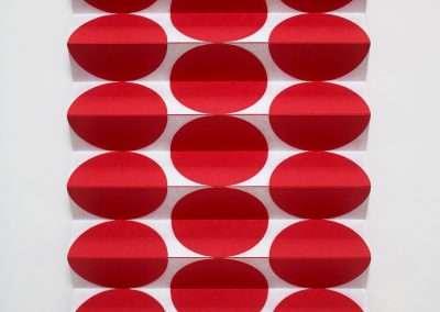 A geometric art piece by Emi Ozawa features a grid of red circular shapes on a white background. The circles are arranged in rows of three, with each row's middle circle appearing indented, creating a visually engaging 3D effect.