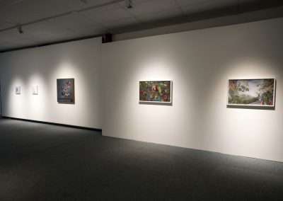 A gallery with white walls displaying four framed artworks by Matthew McConville, illuminated by ceiling lights, with a dark carpeted floor.