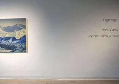 A painting titled "religious journey" by Joanne Lefrak & Hakim Bellamy, depicting snowy mountains, displayed on a gallery wall with the artists' names and title beside it.