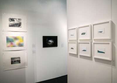 Art gallery interior with white walls displaying various artworks including framed photographs and abstract prints.