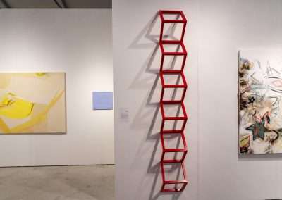 Modern art museum interior showcasing a red ladder-like sculpture mounted on a white wall, with a large abstract yellow painting to the left and a colorful contemporary art canvas to the right.