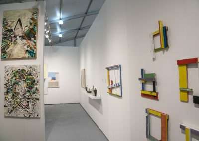 An art gallery interior showcasing various abstract and geometric artworks displayed on white walls, including vividly colored frames and dynamic paintings.
