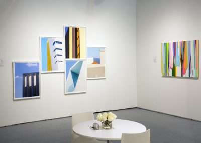 An art gallery interior with a white table and flowers in the foreground, and walls displaying colorful abstract paintings.