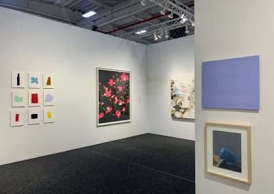 Interior of an art gallery displaying diverse artworks, including abstract pieces, floral prints, and a blue minimalistic canvas, on white walls under bright lighting.