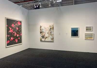 An art gallery with white walls displaying four diverse paintings, including a large one with pink butterflies, surrounded by smaller serene landscapes and abstract pieces.