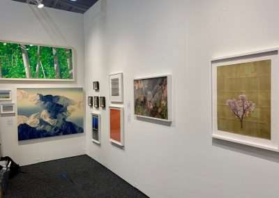 Interior of an art gallery featuring diverse paintings including landscapes and floral scenes, displayed on white walls under bright lighting.