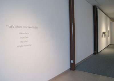 An empty hallway in a building featuring a wall-mounted sign with the text "that's where you need to be" followed by the names william betts, xuan chen, maria park, willy bo richardson.