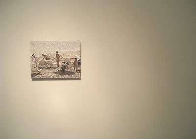 Artwork depicting a crowded beach scene hangs on a plain light-colored wall in a gallery space, illuminated by soft gallery lighting.