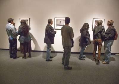 Group of people viewing and discussing framed artworks in a gallery setting.