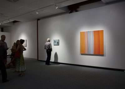 Visitors in an art gallery observing different paintings on white walls, with focused lighting casting soft shadows around the room.