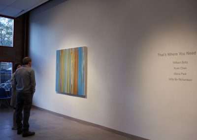 Two people viewing a striped abstract painting in a gallery with artist names listed on the wall to the right.