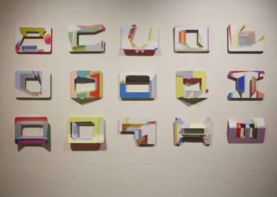 A modern art installation featuring colorful, three-dimensional representations of the alphabet letters hanging on a white wall. each letter has a unique, abstract geometric design.