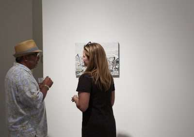 Two people, one wearing a straw hat, engage in conversation while observing a piece of modern art in a gallery.