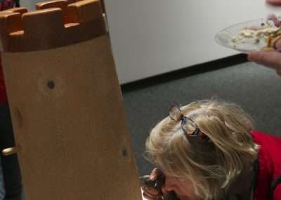 A woman examining a large, cylindrical terracotta sculpture at an art exhibit, using a magnifying glass to closely inspect its texture and details.