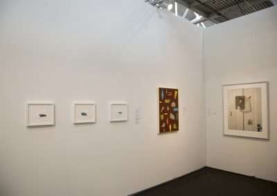 Art gallery interior with plain white walls displaying diverse paintings, including abstract and realistic styles, in a brightly lit exhibition space.