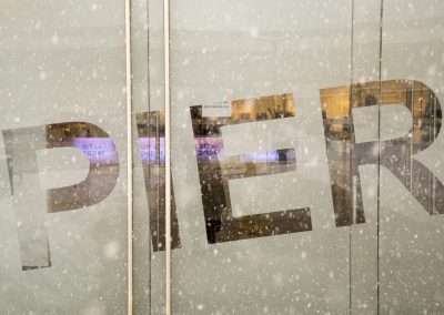 The word "pier" is seen in large, bold letters on a glass door, partially obscured by snowflakes, with a blurred interior visible behind the glass.