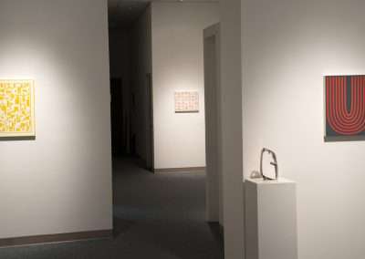 A modern art gallery interior displaying various abstract artworks on white walls, with a sculpture placed on a pedestal in the foreground. the gallery features soft, focused lighting.