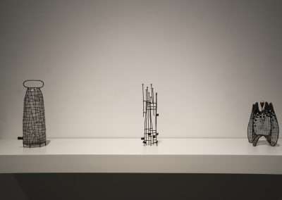 Three abstract wire sculptures displayed on a white shelf against a light grey background, each with differing intricate patterns.