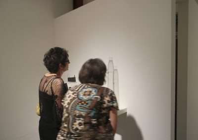 Two women viewing abstract artworks in a gallery, one artwork resembles a tower, ambient lighting with a focus on the art.