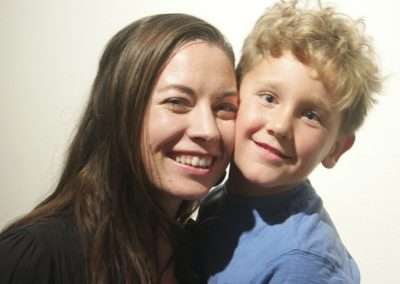 A smiling woman and a young boy with curly hair joyfully posing together.