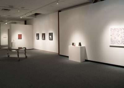 A modern art gallery displaying various artworks on white walls under soft lighting, with a bench in the center for viewing.