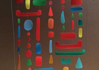 An acrylic panel featuring an arrangement of colorful abstract shapes in various sizes, including rectangles, circles, and elongated forms, suspended in a vertical pattern.