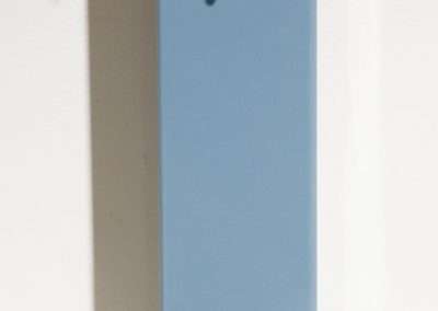 A tall, narrow blue birdhouse with a circular entrance and a small slit below it, mounted on a white wall.