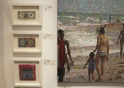 An art gallery display featuring three framed abstract geometric paintings on the left wall and a large mosaic-style piece depicting beachgoers on the right.