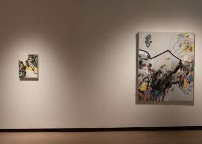Two abstract paintings displayed in a gallery: one large and one small, both featuring vibrant, chaotic brushstrokes on a beige wall with soft lighting.