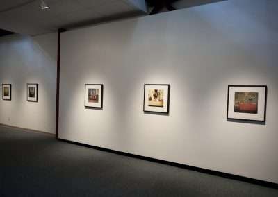 A modern art gallery with four framed photographs evenly spaced on a white wall, illuminated by ceiling spotlights in a dimly lit room.