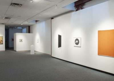 An art gallery interior displaying various paintings and sculptures on bright, white walls. The gallery features a spacious layout with soft lighting, enhancing the visibility of the artworks.