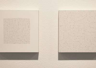 Two square canvases on a wall, each featuring a grid of raised circular elements, one in a dense cluster and the other more evenly spaced, creating textured abstract patterns.