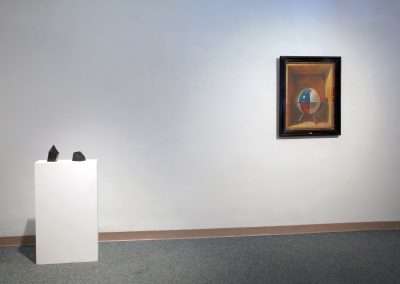 An art gallery interior displaying a framed abstract painting on a gray wall and a white pedestal with two small sculptures to the left.