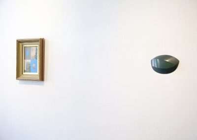 A minimalist white wall featuring a classic framed painting on the left and a modern oval-shaped mirror on the right.