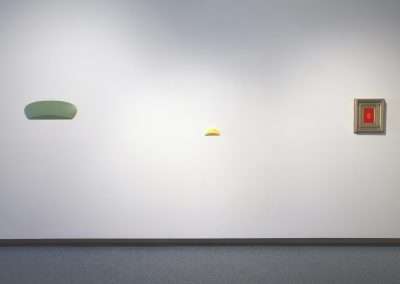 A minimalist art gallery wall displaying three spaced-out items: two abstract, pastel-colored shapes on the left, and a small, framed classical painting on the right.