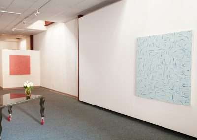 An art gallery with a soft blue and pink abstract painting on white walls, polished floors, and a glass table with flowers in the center.