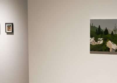 A modern art gallery wall displaying four framed artworks; three smaller pieces in a vertical line on the left and a larger landscape painting on the right, all on a plain white wall with soft lighting.
