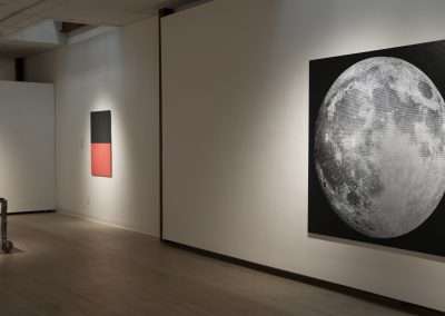 An art gallery interior showing large paintings on white walls, including a prominent realistic painting of the moon to the right. Minimal furniture and soft lighting enhance the artwork display.