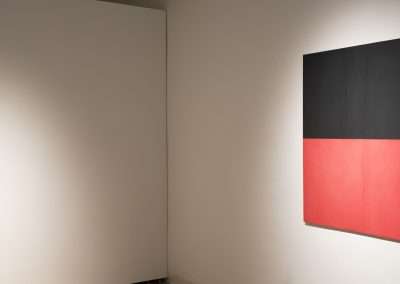 A modern art gallery display featuring a large black and red color-blocked painting on the right and a smaller framed landscape painting on the left.