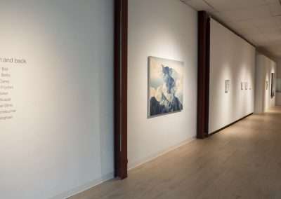 Art gallery interior showing a spacious exhibition hall with a large landscape painting hung on a white wall, with the title "to the moon and back" listed alongside artist names.