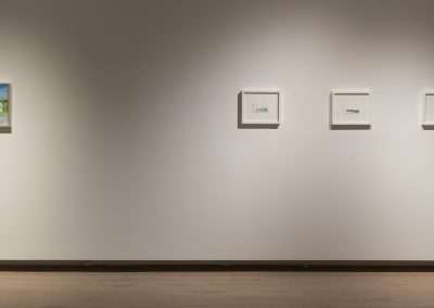 Four framed artworks displayed in a row on a brightly lit gallery wall, featuring minimalistic and abstract styles, with shadows casting on a clean, white surface.