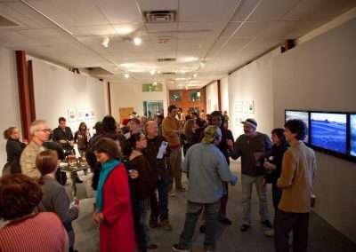 An art gallery filled with people mingling and viewing various artworks. The environment is warm and sociable, with art pieces displayed on well-lit walls.