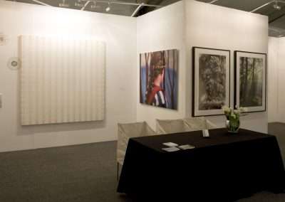 An art gallery display featuring various framed artworks on walls and a central table with floral arrangement and informational brochures.
