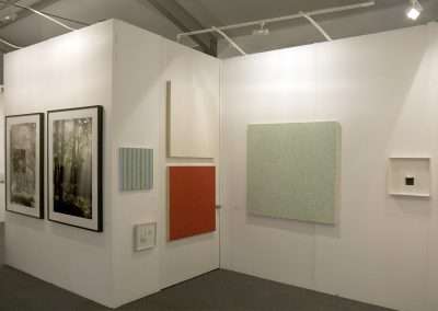 A modern art gallery booth with white walls displaying various abstract and landscape paintings, under bright lighting.