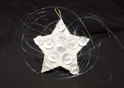 A handmade star-shaped ornament with embedded circular lights, wrapped in delicate silver wires, against a black background.