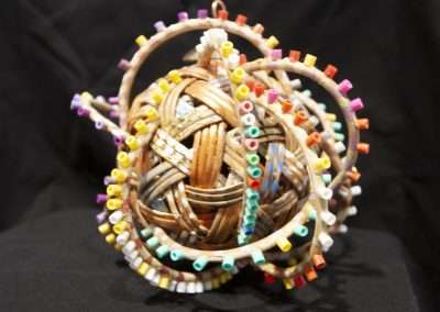 A colorful hand-crafted spherical ornament made of woven straw adorned with multicolored beads, displayed against a black background.
